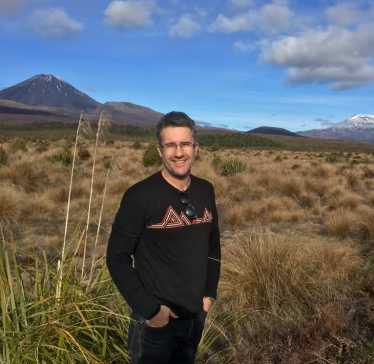 Physiotherapist Greg Bell standing in tussock with Mt Ngauruhoe behind